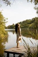 jovem de pé no cais de madeira no lago calmo foto