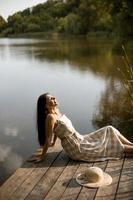 jovem relaxante no cais de madeira no lago calmo foto