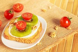 torrada com kiwi, queijo e tomate cereja em um pedaço de saco em tábua de madeira. foto