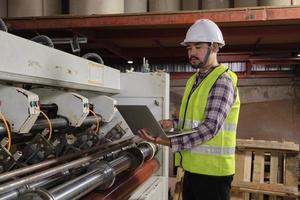 engenheiro de manutenção masculino asiático em uniforme de segurança e capacete, inspeção de qualidade por laptop, verifique a máquina na indústria de fabricação de produção de papel e papelão, gerente de trabalhador técnico de fábrica. foto