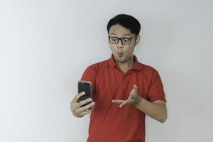 uau cara de jovem asiático chocou o que vê no smartphone em fundo cinza isolado. foto