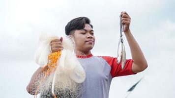 feliz jovem pescador na praia segurando seu peixe e mostra na frente de seu barco foto