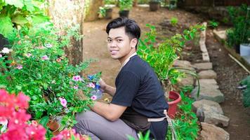 homem asiático cuidando de regar flores no jardim de casa foto