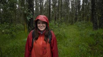 mulher hispânica com mochila preta e jaqueta impermeável vermelha andando em uma trilha lamacenta por uma floresta durante o dia foto