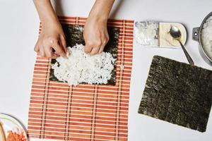 chef de mulher enchendo rolos de sushi japonês com arroz foto