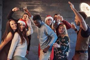 festa com amigos. eles amam o natal. grupo de jovens alegres carregando estrelinhas e taças de champanhe, dançando na festa de ano novo e parecendo feliz. conceitos sobre estilo de vida de união foto