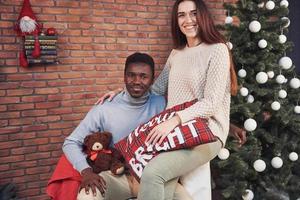 jovem casal multiétnico, reunião de Natal, abraços em casa. ano Novo. clima festivo de um homem e uma mulher foto