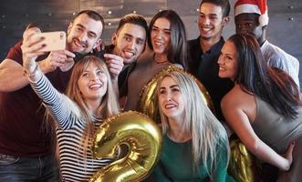 grupo de jovens lindos fazendo selfie na festa de ano novo, melhores amigos, meninas e meninos juntos, se divertindo, posando de pessoas de estilo de vida emocional. chapéus de Papai Noel e taças de champanhe nas mãos foto