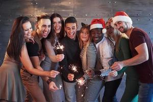 festa com amigos. grupo de jovens alegres carregando estrelinhas e taças de champanhe foto