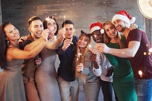 festa com amigos. grupo de jovens alegres carregando estrelinhas e taças de champanhe foto