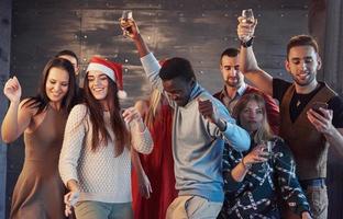 festa com amigos. eles amam o natal. grupo de jovens alegres carregando estrelinhas e taças de champanhe, dançando na festa de ano novo e parecendo feliz. conceitos sobre estilo de vida de união foto