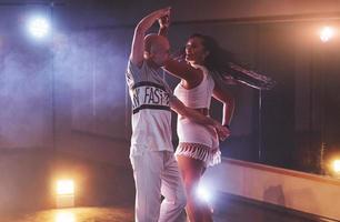 dançarinos habilidosos se apresentando no quarto escuro sob a luz e a fumaça do show. casal sensual realizando uma dança contemporânea artística e emocional foto