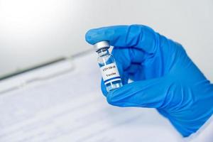 garrafa de vacina de coronavírus covid-19 para injeção na mão de médico ou cientista técnico em traje de proteção, saúde antiviral e conceito de risco biológico médico foto