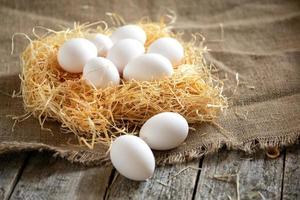 ovos de galinha branca no ninho de palha em uma serapilheira em tábuas de madeira foto