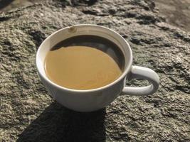 xícara branca de café cremoso isolado no fundo de pedra foto