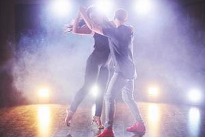 dançarinos habilidosos se apresentando no quarto escuro sob a luz e a fumaça do show. casal sensual realizando uma dança contemporânea artística e emocional foto