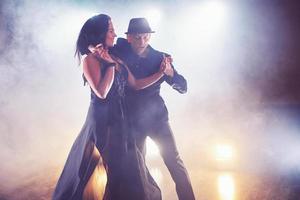 dançarinos habilidosos se apresentando no quarto escuro sob a luz e a fumaça do show. casal sensual realizando uma dança contemporânea artística e emocional foto