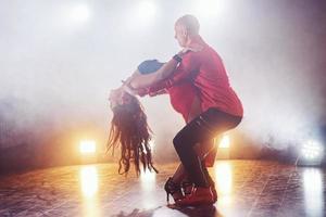 dançarinos habilidosos se apresentando no quarto escuro sob a luz e a fumaça do show. casal sensual realizando uma dança contemporânea artística e emocional foto