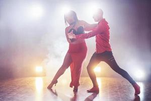 dançarinos habilidosos se apresentando no quarto escuro sob a luz e a fumaça do show. casal sensual realizando uma dança contemporânea artística e emocional foto