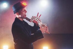 mágico mostrando truque com cartas de baralho. magia ou destreza, circo, jogo. prestidigitador em quarto escuro com neblina foto