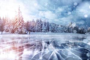 gelo azul e rachaduras na superfície do gelo. lago congelado nas montanhas de inverno. está nevando. as colinas de pinheiros. inverno. cárpatos ucrânia europa foto