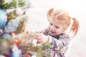 feliz natal e boas festas. jovem ajudando a decorar a árvore de natal, segurando algumas bolas de natal na mão foto