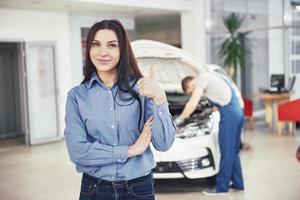 a mulher aprova o trabalho feito pelo cliente. o mecânico trabalha sob o capô do carro foto