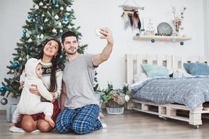 família reunida em torno de uma árvore de natal, usando um tablet foto