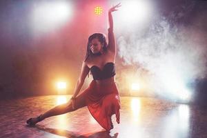 dançarina habilidosa e bonita se apresentando no quarto escuro sob a luz e a fumaça do show, realizando uma dança contemporânea artística e emocional foto