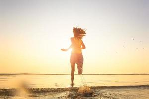 mulher correndo para o mar à luz do sol da manhã. foto