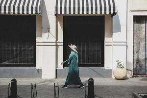 mulher de chapéu de verão e vestido verde andando e passando a loja na área comercial foto