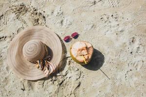 vista superior do chapéu de verão e óculos de sol com coco isolado no fundo da areia da praia foto