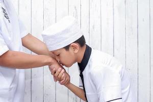 menino muçulmano cumprimentando e pedindo perdão beijando a mão no ramadan e eid mubarak foto