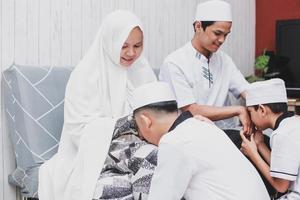 família asiática com vestido tradicional perdoando uns aos outros na celebração de eid mubarak as crianças beijando os pais de mãos dadas foto
