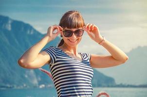 menina bonita com camisa listrada colocar óculos de sol e sorrir na frente do lago leman genebra foto