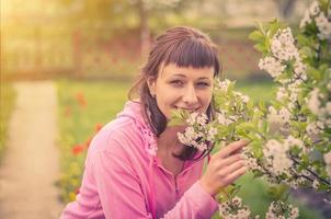 jovem mulher bonita olhando para a câmera, sorrindo e cheirando flores de cerejeira foto