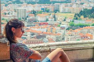 jovem viajante bonita com óculos de sol está cruzando os braços e sentado na varanda do castelo medieval de leiria foto