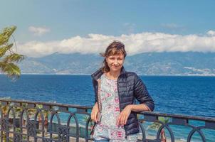 jovem e bela viajante olhando a câmera, sorrindo e posando no aterro lungomare falcomata em reggio calabria foto