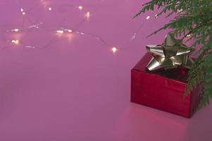 caixa vermelha festiva concert.gift debaixo da árvore de natal em um fundo rosa com uma guirlanda. feche o espaço da cópia. cartão postal de férias. foto