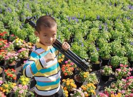 menino asiático carregando tripés em pé no jardim de flores foto