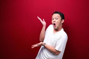 jovem asiático está surpreso e gritando uau com o direito de apontar com a mão isolada no fundo vermelho. foto