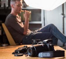 câmera e equipamento em cima da mesa no estúdio no fundo do fotógrafo sentado foto