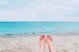 pés de mulher com unhas vermelhas no fundo da beira-mar foto