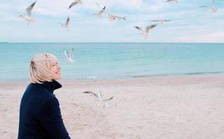 mulher loira e gaivotas em dia nublado na costa do mar foto