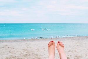 pés de mulher com unhas vermelhas no fundo da beira-mar foto
