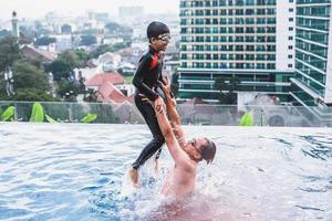 pai pegando seu filho que está pulando na piscina