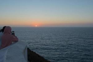 grupo de pessoas irreconhecíveis olhando o pôr do sol e tirando fotos com seus celulares. Cabo de São Vicente, Fim da Europa. Portugal.