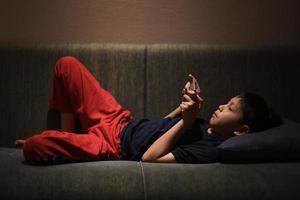 menino asiático deitado no sofá enquanto jogava no smartphone antes de dormir foto