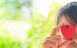 mulher asiática jovem feliz segurando corações vermelhos olhos fechados na natureza bokeh verde borrão background - no amor dia dos namorados e conceito de caridade foto