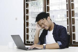 jovem asiático se sentindo estressado e confuso quando trabalha laptop na mesa. foto